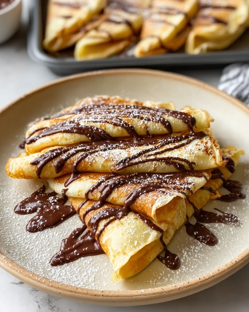 The image shows a plate of golden, folded crepes drizzled generously with chocolate sauce and dusted lightly with powdered sugar, creating a visually appealing and indulgent dessert. The crepes are neatly stacked on a beige ceramic plate, with some chocolate sauce artistically spread on the plate itself. In the background, more crepes can be seen on a tray, enticingly similar in presentation. The soft texture of the crepes combined with the rich chocolate drizzle invites the viewer to savor this sweet treat. photo taken with an iPhone --ar 4:5 --v 7