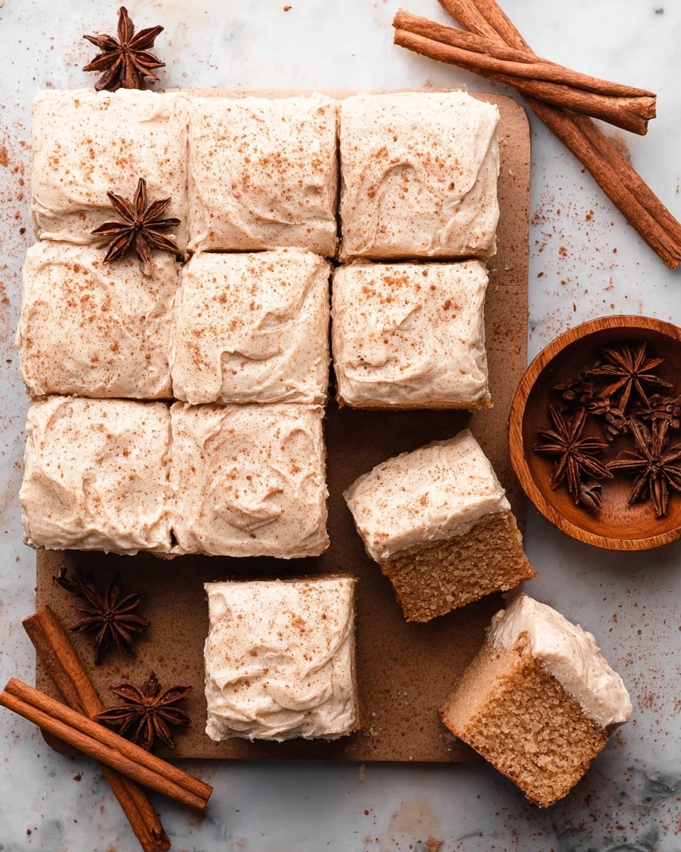 A grid of nine square cake pieces is shown on a white marbled surface, each topped with a thick layer of creamy beige frosting sprinkled lightly with cinnamon powder. The cake itself is light brown with a moist and fluffy texture visible on the two pieces pulled away from the grid. Nearby, a small round wooden bowl holds whole star anise and cinnamon sticks, adding warm, rustic tones. Two cinnamon sticks and two star anise pods rest on the surface next to the cake, completing a cozy, spiced look. Photo taken with an iphone --ar 4:5 --v 7