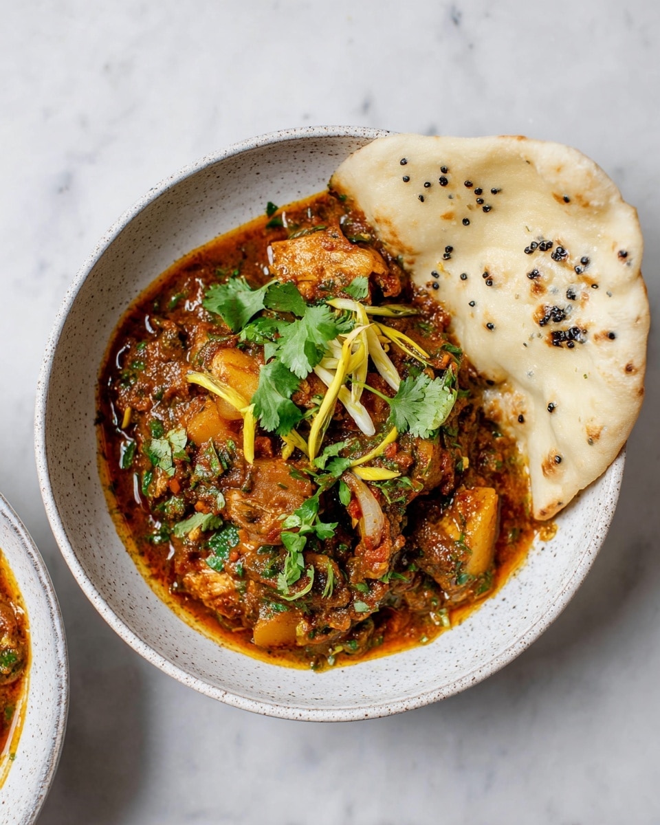 A white speckled bowl holds a rich, thick stew with a deep orange-brown sauce. The stew contains visible pieces of cooked chicken, sliced potatoes, and tomatoes mixed with finely cooked onions and spices. Bright green chili peppers and fresh cilantro leaves sprinkle the top, along with thin pale yellow ginger strips. A large piece of soft, pale flatbread with black sesame dots rests on the edge of the bowl, partially dipped into the stew. The bowl sits on a white marbled surface. photo taken with an iphone --ar 4:5 --v 7