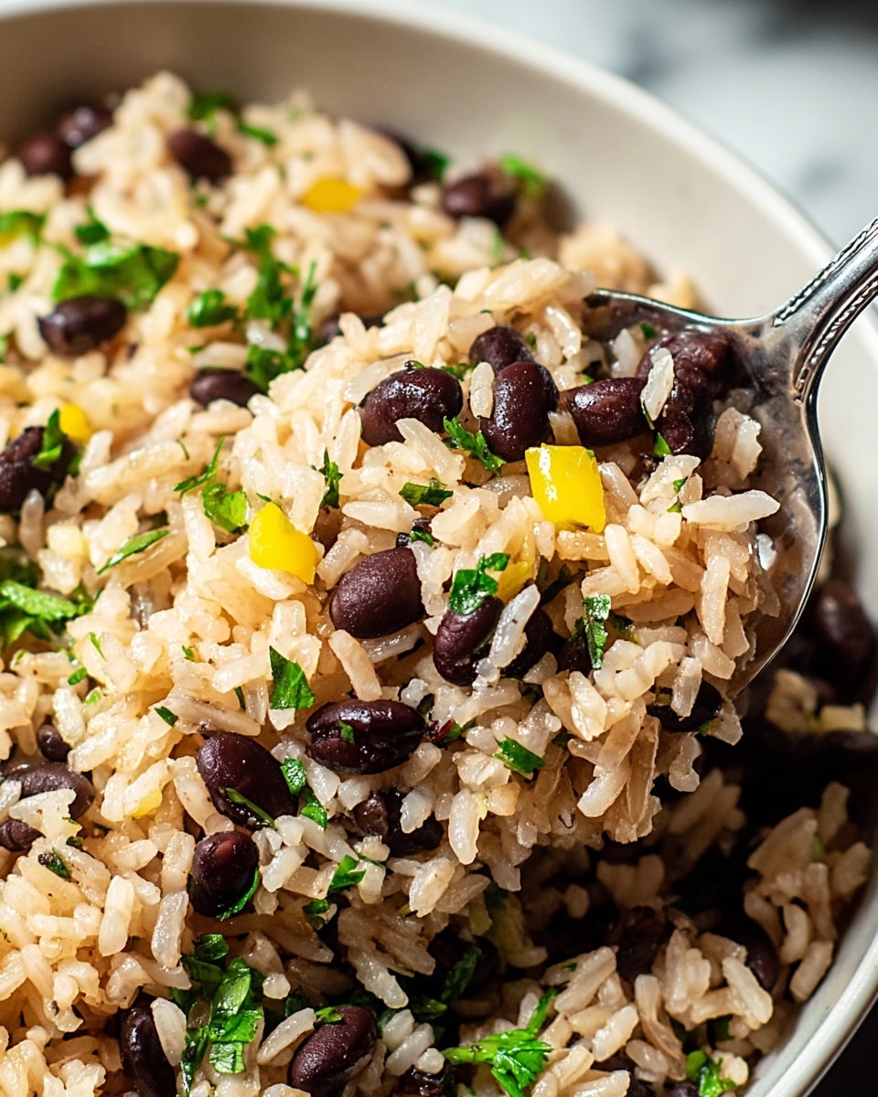 A close-up image of cooked rice mixed with small black beans and green parsley pieces scattered throughout, with some yellow bell pepper bits adding color contrast; the rice grains look soft and fluffy with a light brown tint, and the dish is served in a white bowl with a silver spoon lifting a portion, all set against a white marbled background. photo taken with an iphone --ar 4:5 --v 7