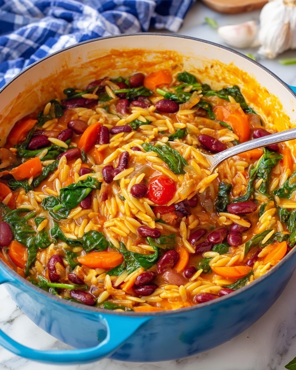 The image shows a close-up of a blue pot filled with a colorful cooked dish made of several visible layers: the first layer is a yellow-orange thick sauce, followed by light yellow orzo pasta spread throughout, then dark red kidney beans and light brown beans scattered across the dish, bright orange sliced carrots, and vibrant green spinach leaves mixed evenly inside. Whole small red cherry tomatoes add a pop of color. A silver spoon is scooping some of the mixture from the pot. The pot sits on a white marbled surface with a blue and white checkered cloth and a garlic bulb in the background. photo taken with an iphone --ar 4:5 --v 7