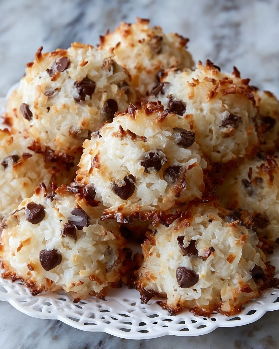A close-up view of three coconut macaroon cookies stacked on white parchment paper, each cookie with a rough, lumpy texture made of shredded white coconut mixed with dark chocolate chips. The edges of the cookies are golden-brown and slightly crispy, while the inside remains soft and white with visible chocolate pieces. There are a few large white coconut flakes scattered on top and around the cookies. The background is softly blurred to keep focus on the cookies. photo taken with an iphone --ar 4:5 --v 7
