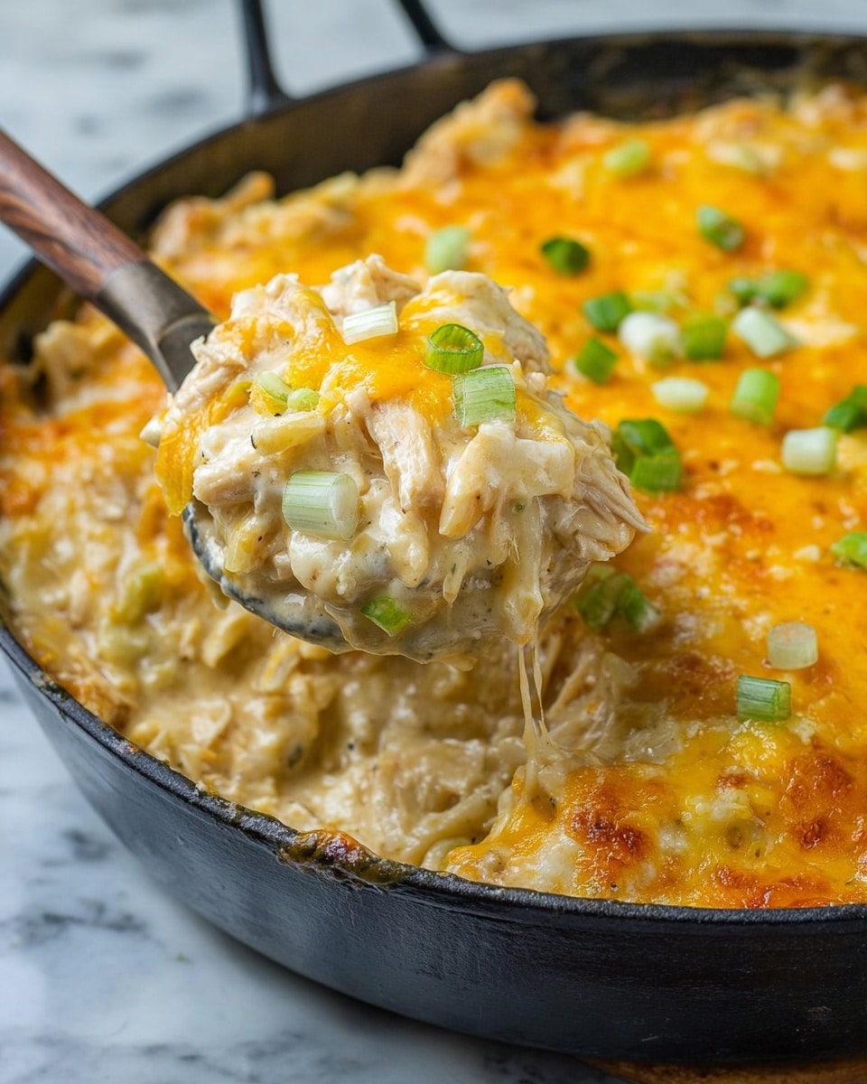 A close-up of a creamy, cheesy dish in a black pan, showing a spoon lifting a thick scoop. The dish has three main layers: a base layer of creamy, white sauce mixed with chunks of tender chicken and pasta, a middle layer of melted yellow and orange cheese creating a bubbly, slightly browned surface, and small green pieces of chopped green onion sprinkled on top. The textures include a smooth sauce, tender chicken, soft pasta, and gooey cheese, all mixed together with an evenly browned top layer. The background shows a white marbled surface. photo taken with an iphone --ar 4:5 --v 7