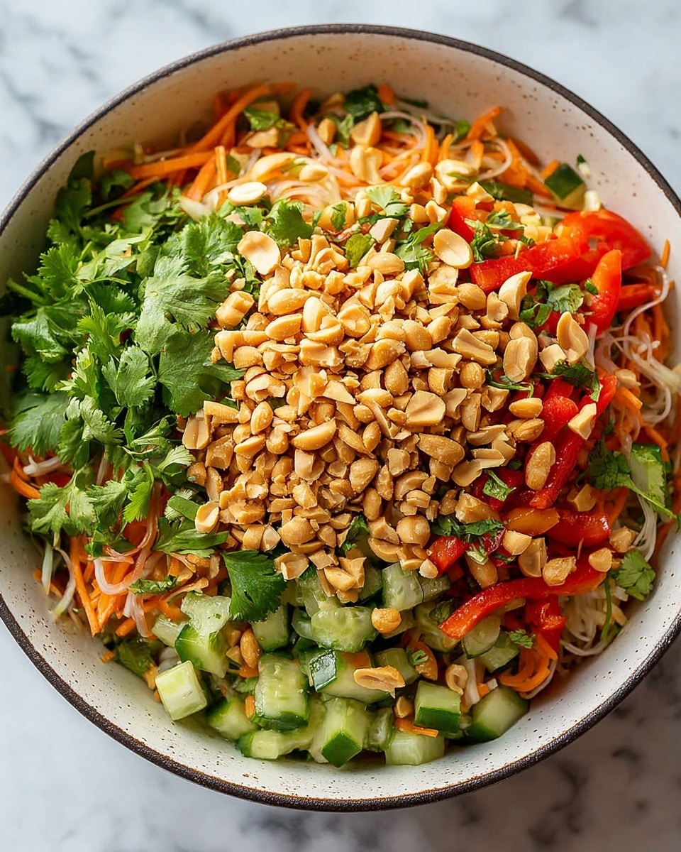 A bowl filled with a colorful salad showing several layers: at the bottom, there are chopped cucumber pieces, red bell pepper slices, and shredded carrots mixed with clear, thin noodles. Above this base mix, there is a generous layer of chopped cilantro leaves spread evenly. The top layer is covered with a heap of crushed peanuts, light brown and textured, sprinkled all over the salad. The bowl is white with a slightly speckled texture and a thin dark rim, sitting on a white marbled surface. photo taken with an iphone --ar 4:5 --v 7