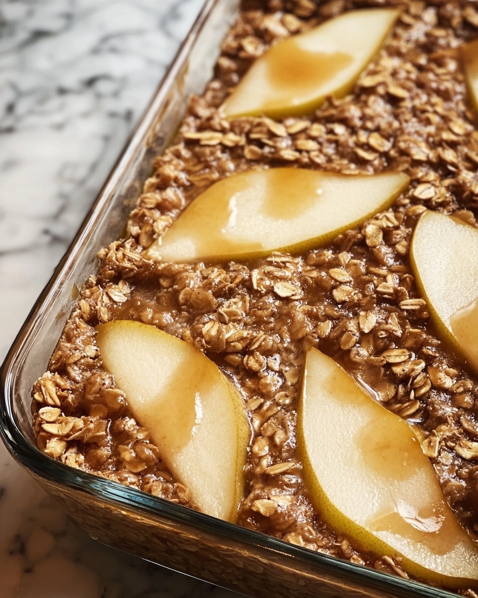 The dish is a baked oat dessert in a clear glass rectangular baking dish, showing a single thick layer of cooked oats mixed with a brown cinnamon sauce. On the surface, there are evenly placed thin slices of light yellow pear with smooth skin, partially submerged in the oat mixture. The texture looks soft and slightly sticky with whole oats visible, and the edges are slightly raised and browned. The background is a kitchen scene with a white marbled texture in the foreground. Photo taken with an iphone --ar 4:5 --v 7