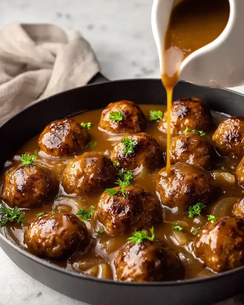 The image shows a black skillet filled with golden-brown meatballs covered in a thick, glossy brown gravy. The meatballs are scattered across the skillet, partially dipped into the gravy that has a smooth texture and includes translucent cooked onions. Small sprigs of bright green parsley are sprinkled on top of the meatballs and gravy, adding a fresh color contrast. In the background, there is a white jug pouring more gravy, with a drop running down the side, set on a white marbled surface. photo taken with an iphone --ar 4:5 --v 7