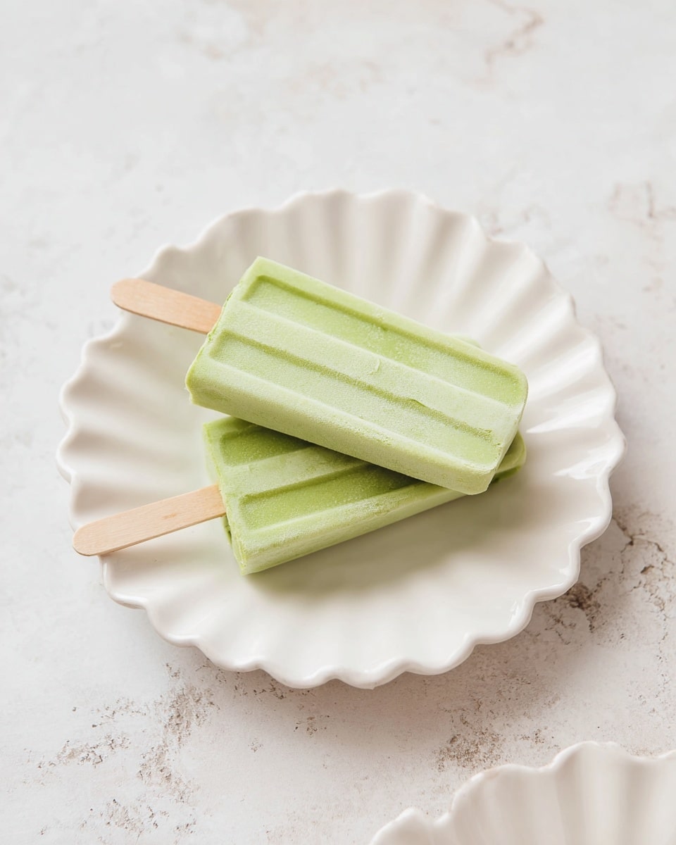 The image shows three light green popsicles stacked in the center of a white scalloped plate with a soft, slightly frosted texture on the popsicles' surface. The popsicles have smooth edges and wooden sticks visible at one end, lying on top of each other with two on the bottom and one on top diagonally. The plate rests on a white marbled surface that adds subtle texture to the background, with parts of two other white scalloped plates slightly visible at the edges of the frame. photo taken with an iphone --ar 4:5 --v 7
