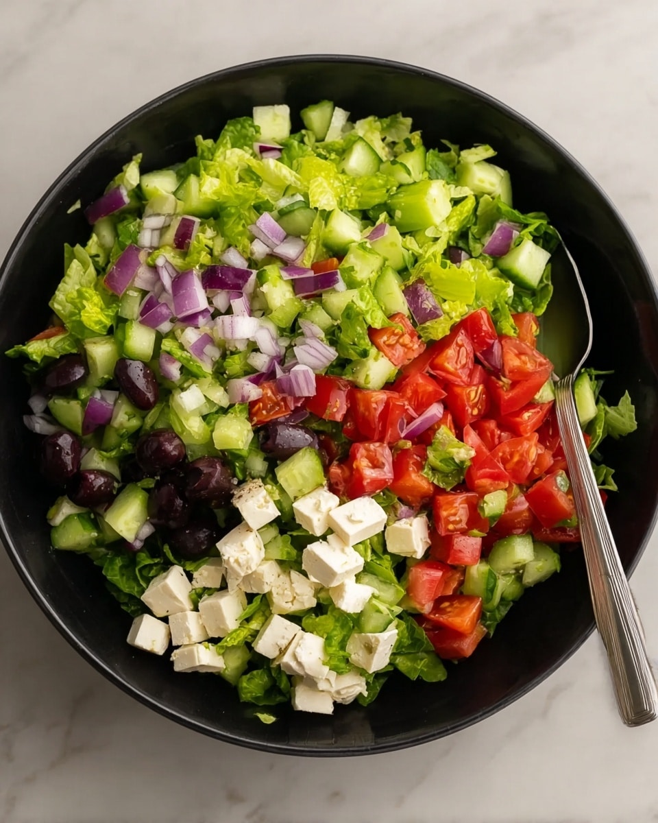 A black bowl filled with a fresh salad that has four main layers: a base of bright green chopped lettuce, scattered with small cubes of white cheese with a smooth texture; then pieces of red tomato chunks and dark black olives sprinkled evenly; the top layer includes diced green cucumber with light green skin and purple-red chopped onion bits. A silver spoon is placed inside the bowl on the right side. The bowl sits on a white marbled surface. photo taken with an iphone --ar 4:5 --v 7